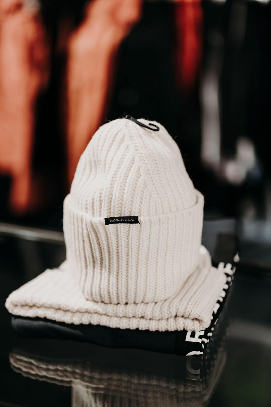 Weiße Strickmütze mit Etikett auf gefalteter Kleidung im Hintergrund