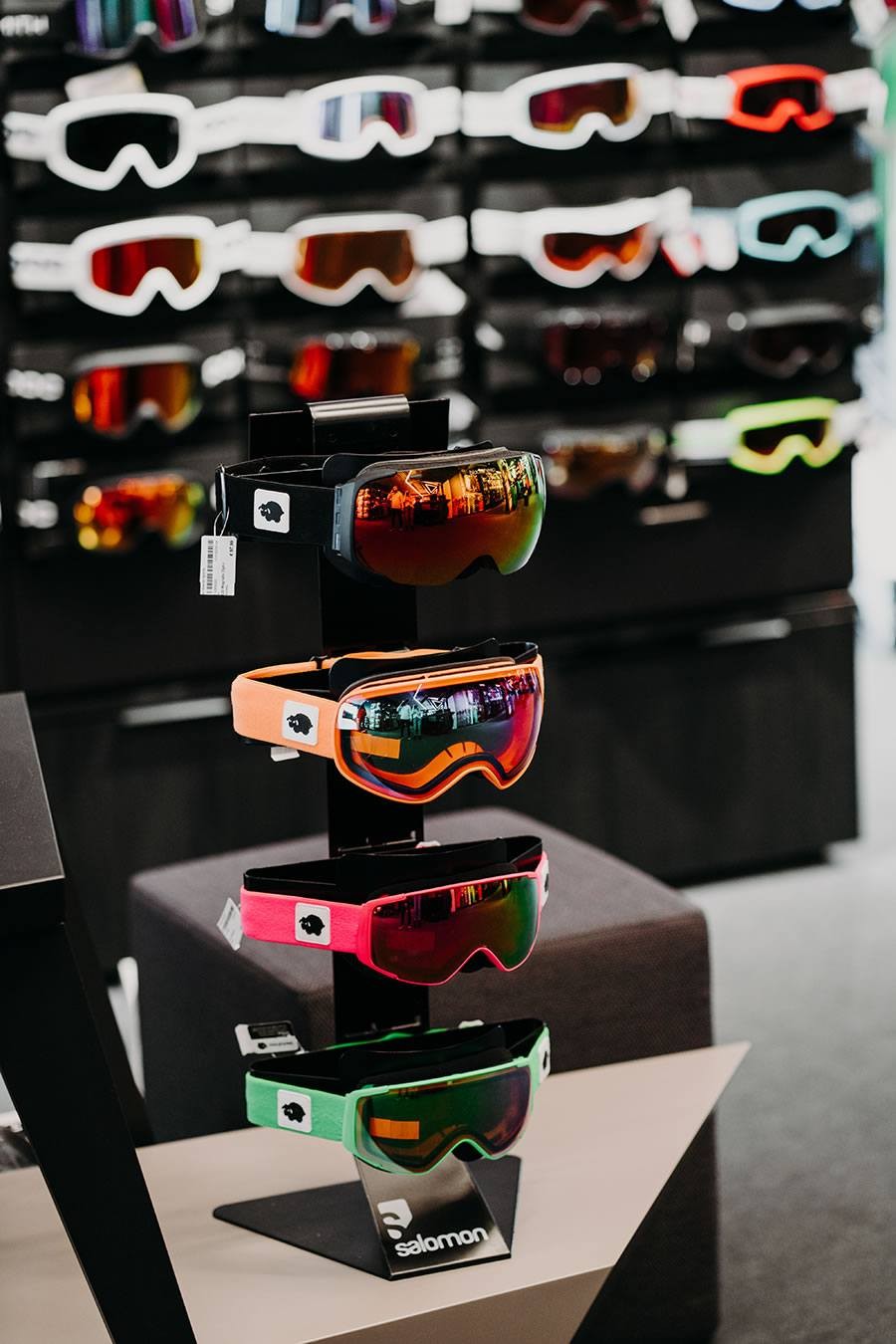 Drei bunte Skibrillen auf einem schwarzen Ständer im Geschäft ausgestellt