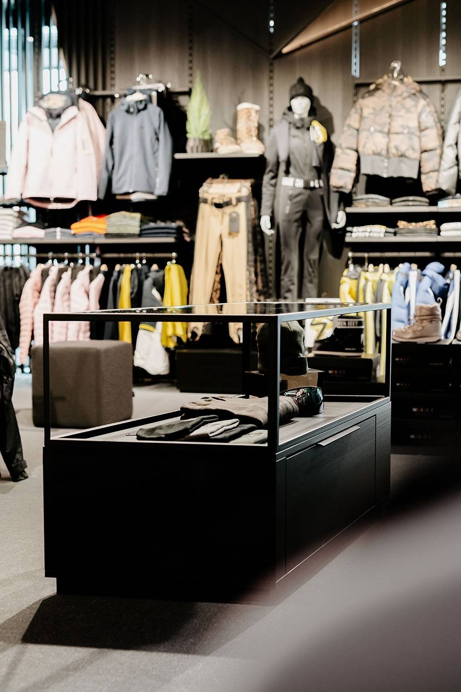 Bekleidungsgeschäft mit ausgestellten Jacken, Hosen und Accessoires auf Regalen und einem Tisch